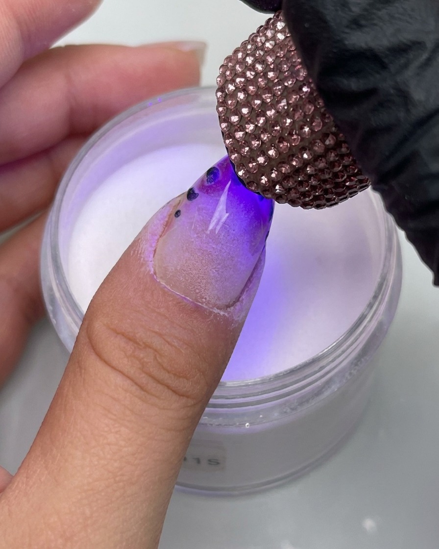 Gros plan dun doigt avec un design léopard placé sous une lampe UV décorée de strass.