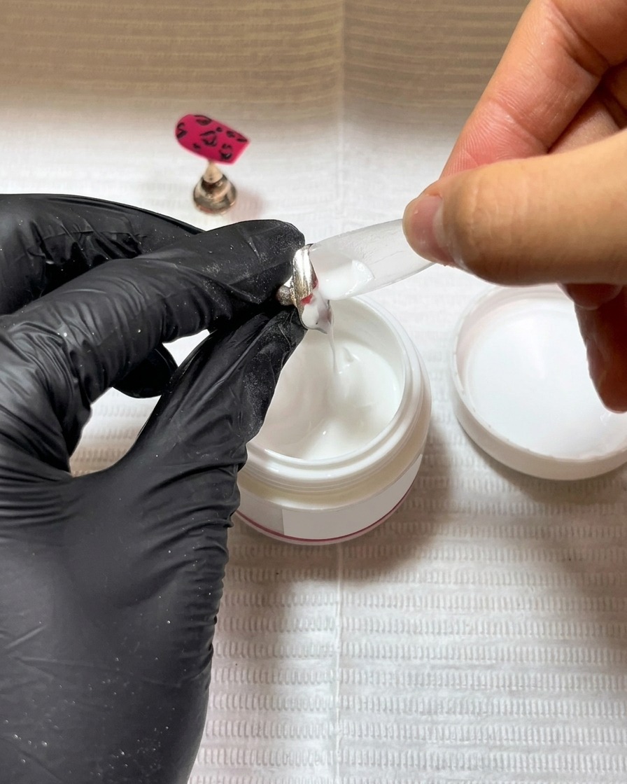 Un pinceau appliquant une fine couche de base coat en gel noir sur une capsule propre.