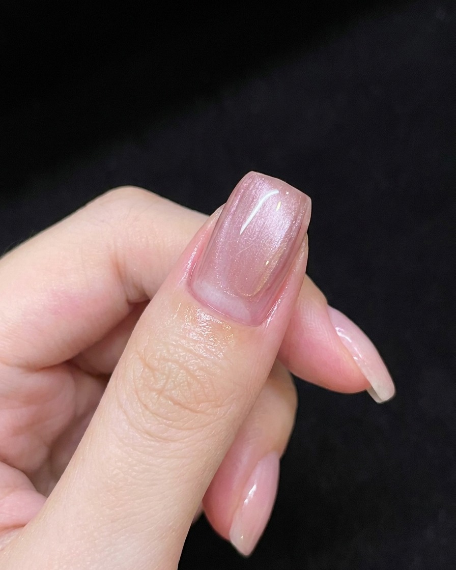 Une main tenant un aimant au-dessus dun ongle recouvert de gel rose pour créer une ligne scintillante.