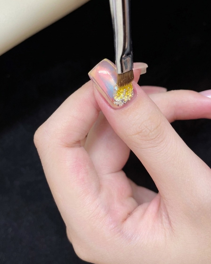 Un pinceau appliquant une goutte de gel adhésif transparent sur la base de longle.