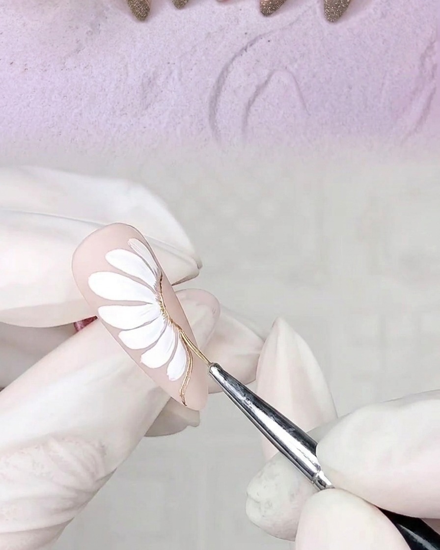 Une main avec un ongle décoré placée dans une lampe UV pour catalyser les contours en gel adhésif fraîchement appliqués.