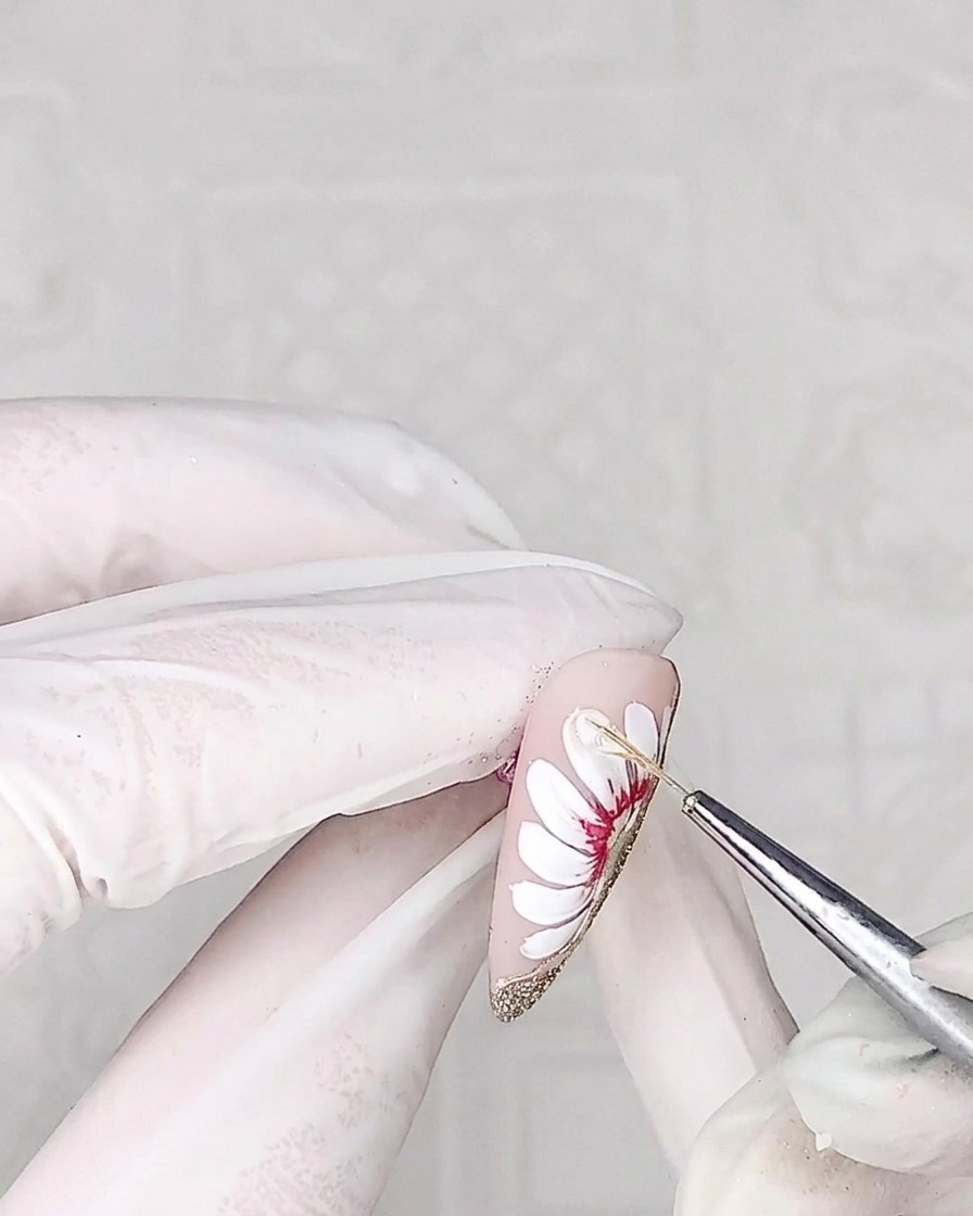 Gros plan dun pinceau liner appliquant un gel adhésif épais et transparent sur la surface dun pétale de marguerite.