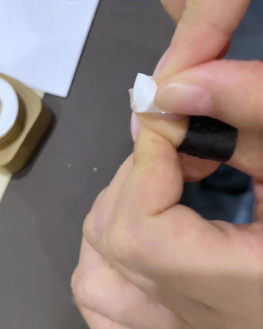 Gros plan dune main appliquant un petit morceau de ruban correcteur blanc autour de la cuticule.