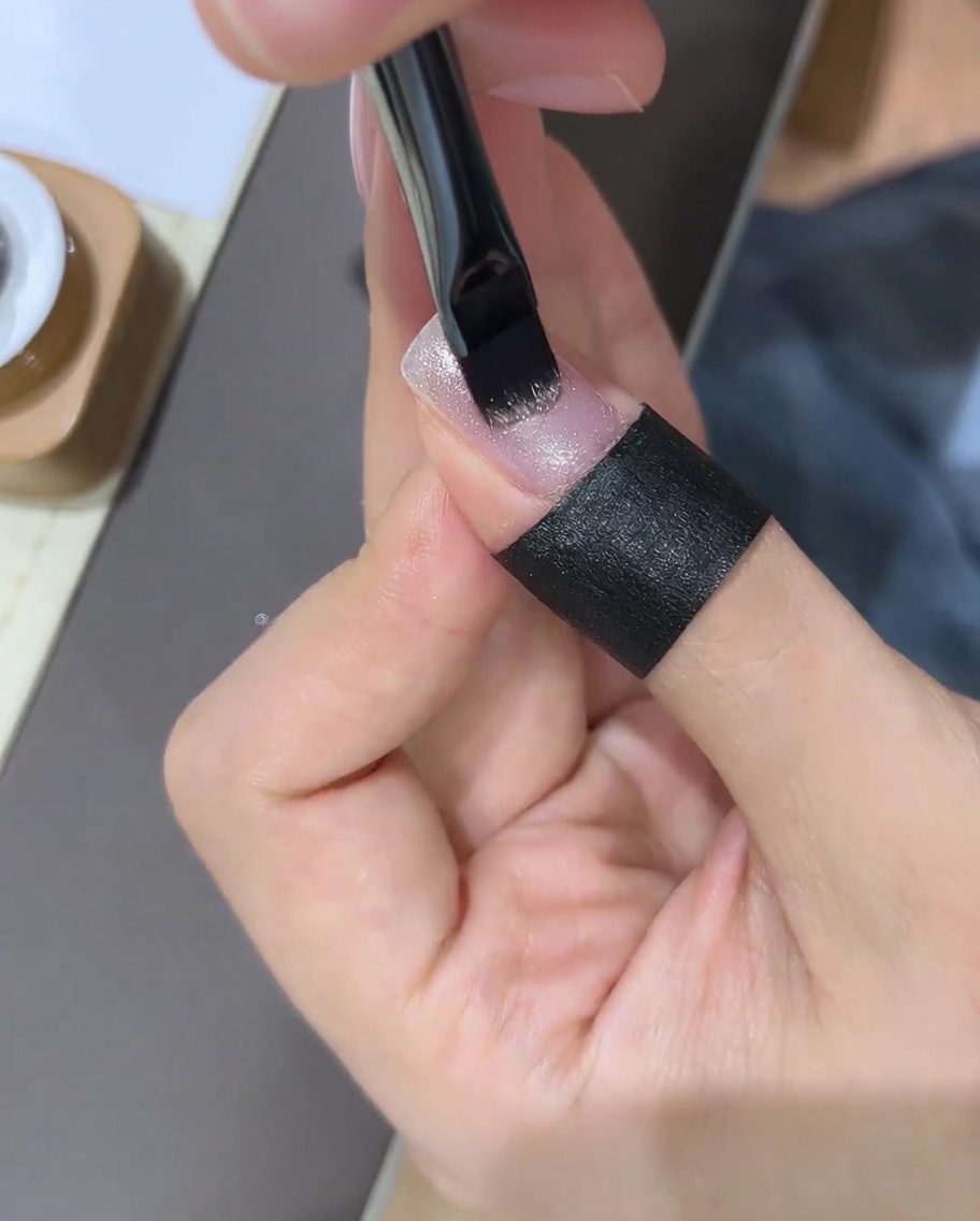 Une main utilisant un aimant à ongles au-dessus dun ongle en gel fraîchement peint pour manipuler les particules de paillettes.