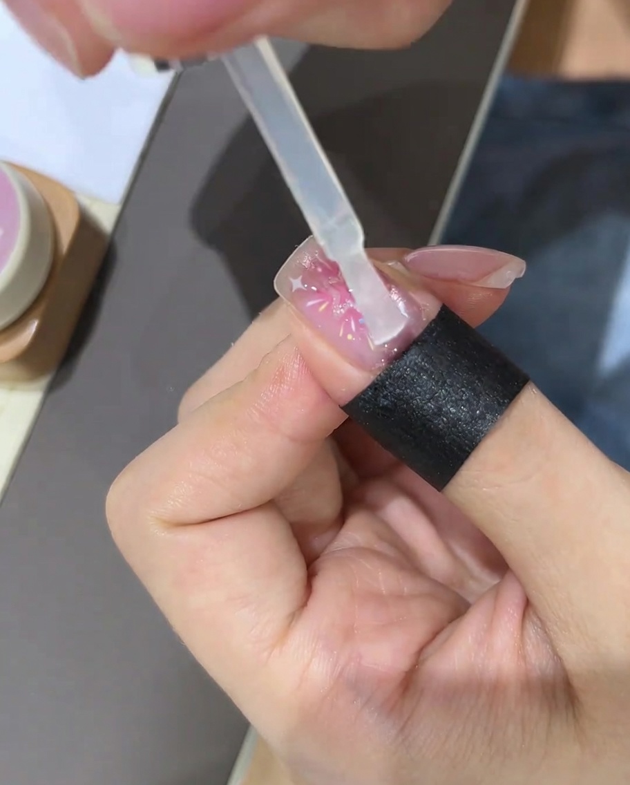 Un pinceau appliquant un top coat transparent sur le design dongle étoilé terminé.