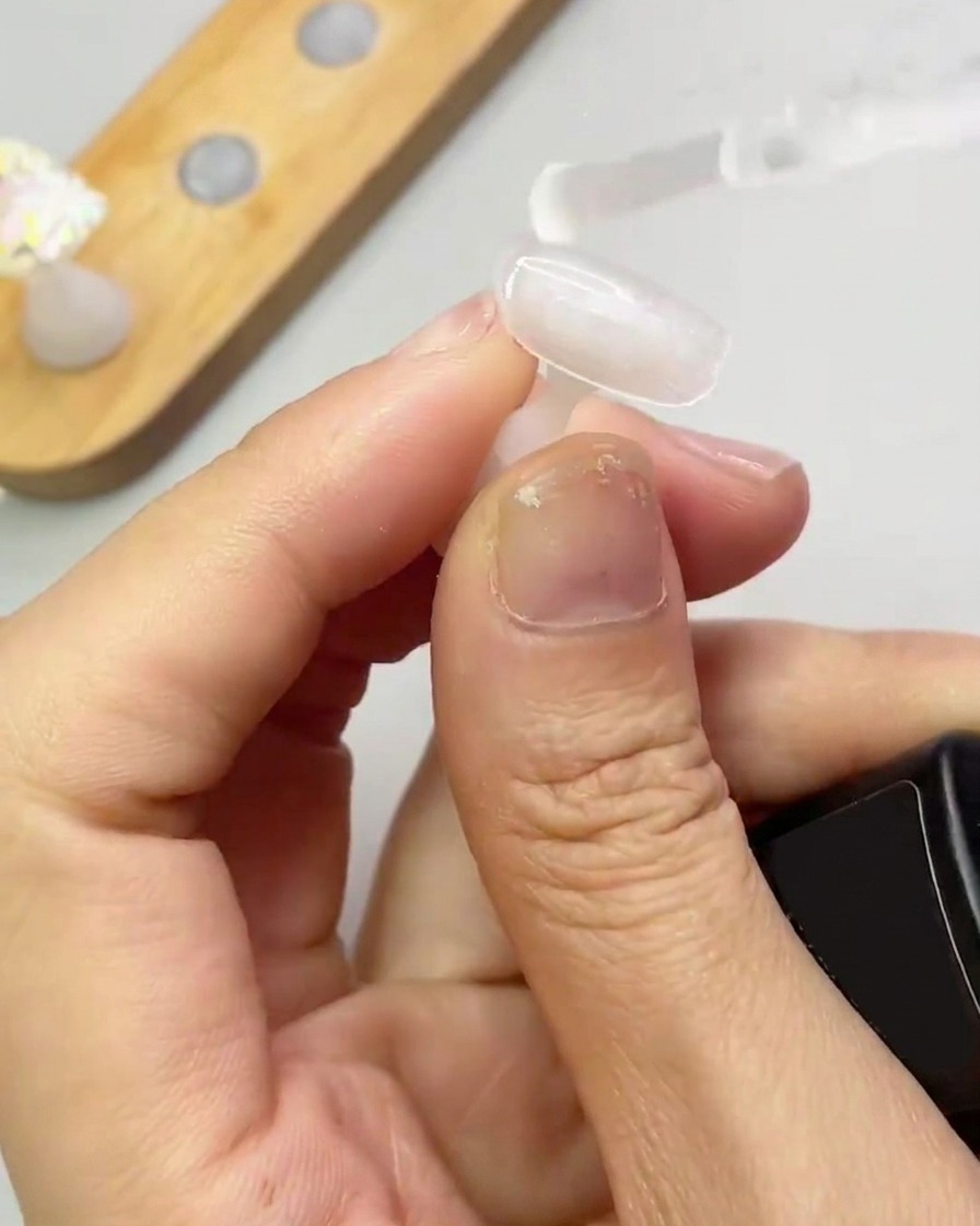 Un pinceau applique une fine couche transparente de gel de renforcement sur un ongle.