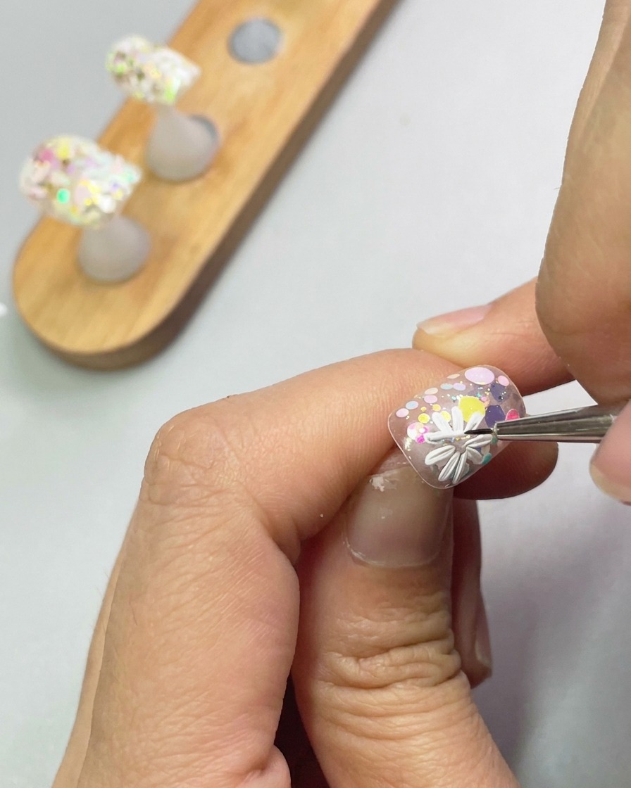Vue rapprochée dun pinceau utilisant du gel de modelage blanc pour former les pétales dune deuxième petite marguerite sur longle.