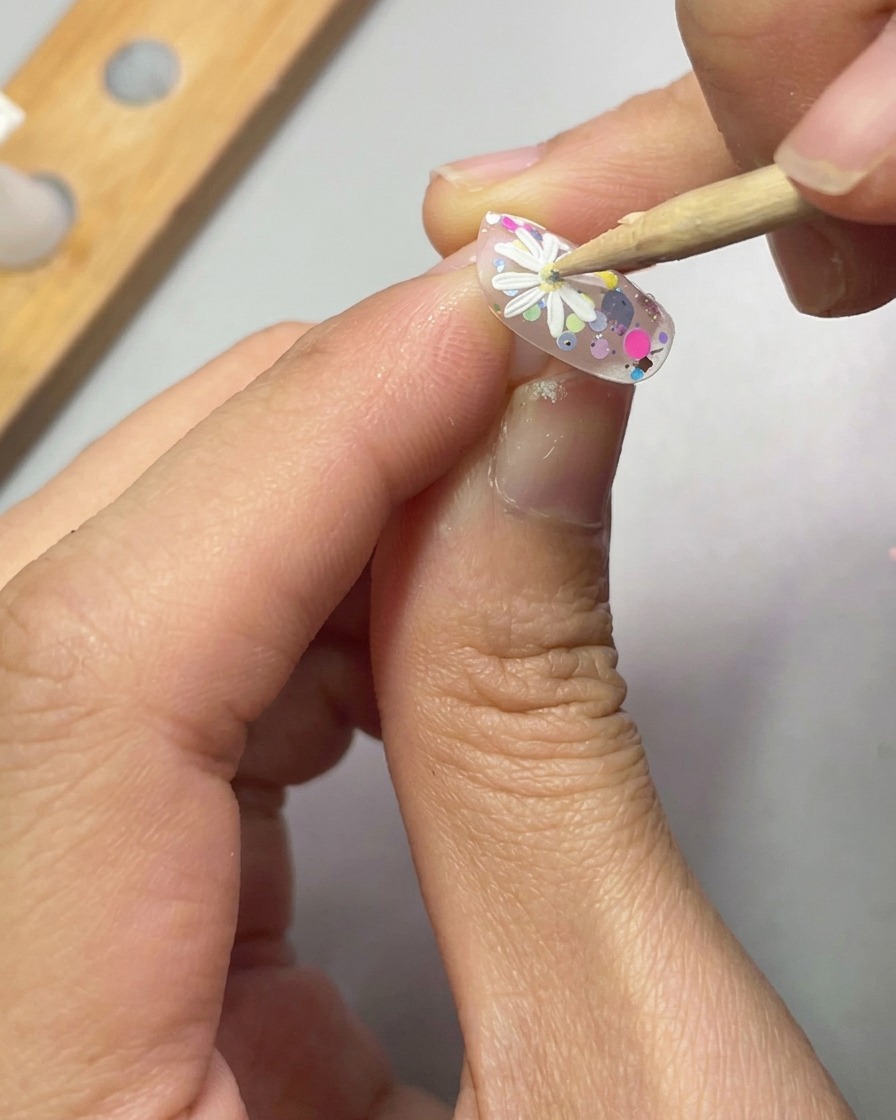 Un outil de dotting place une petite goutte de gel jaune au centre dune marguerite blanche 3D.