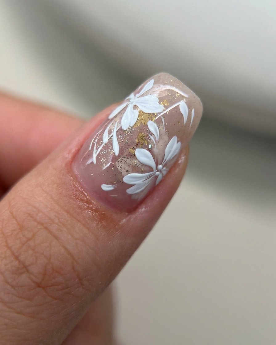 Gros plan sur un ongle avec une teinte rose nude transparente recouverte dune fine couche de paillettes dorées.