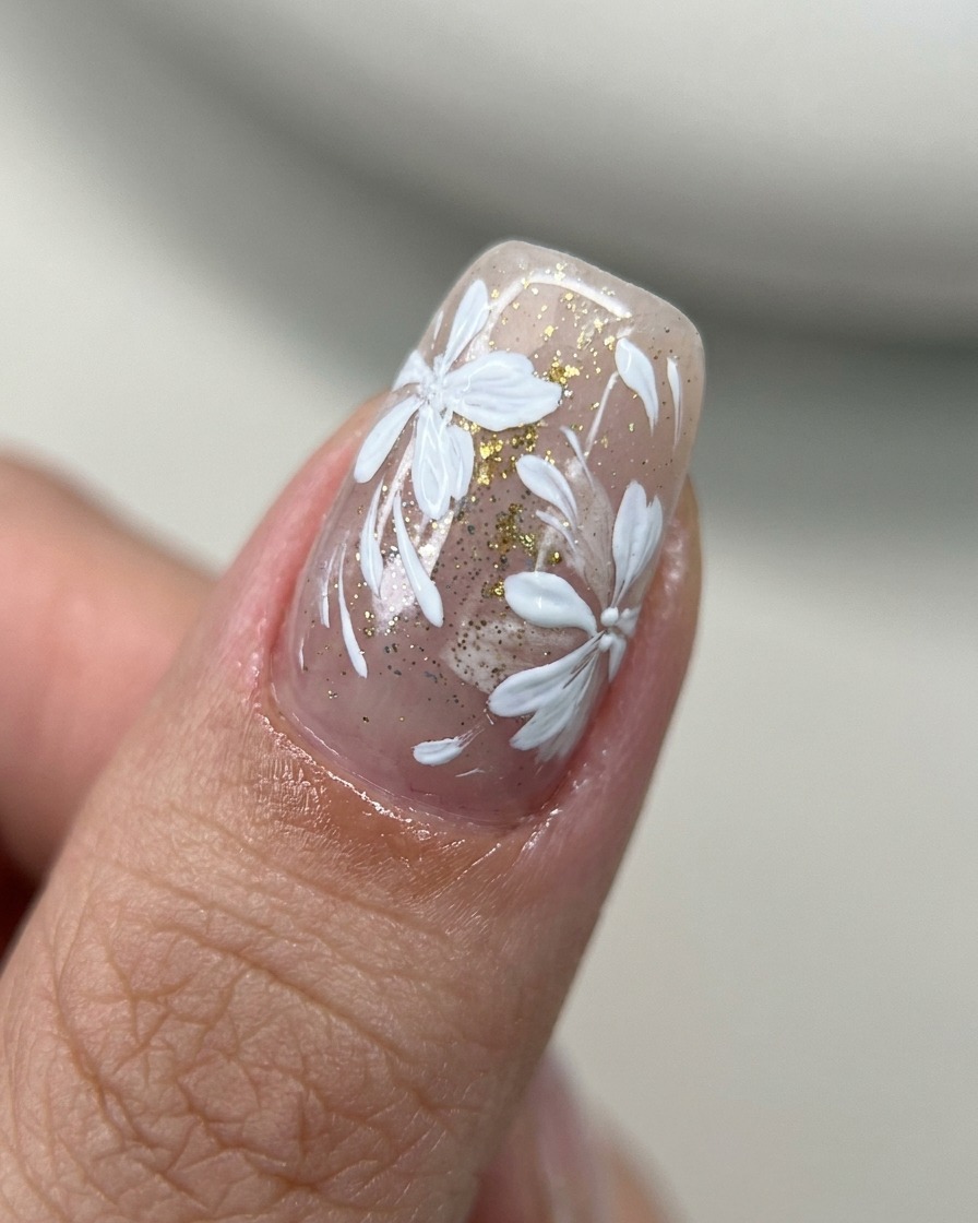 Un pinceau applique un top coat transparent sur un ongle décoré de motifs floraux et dorés.