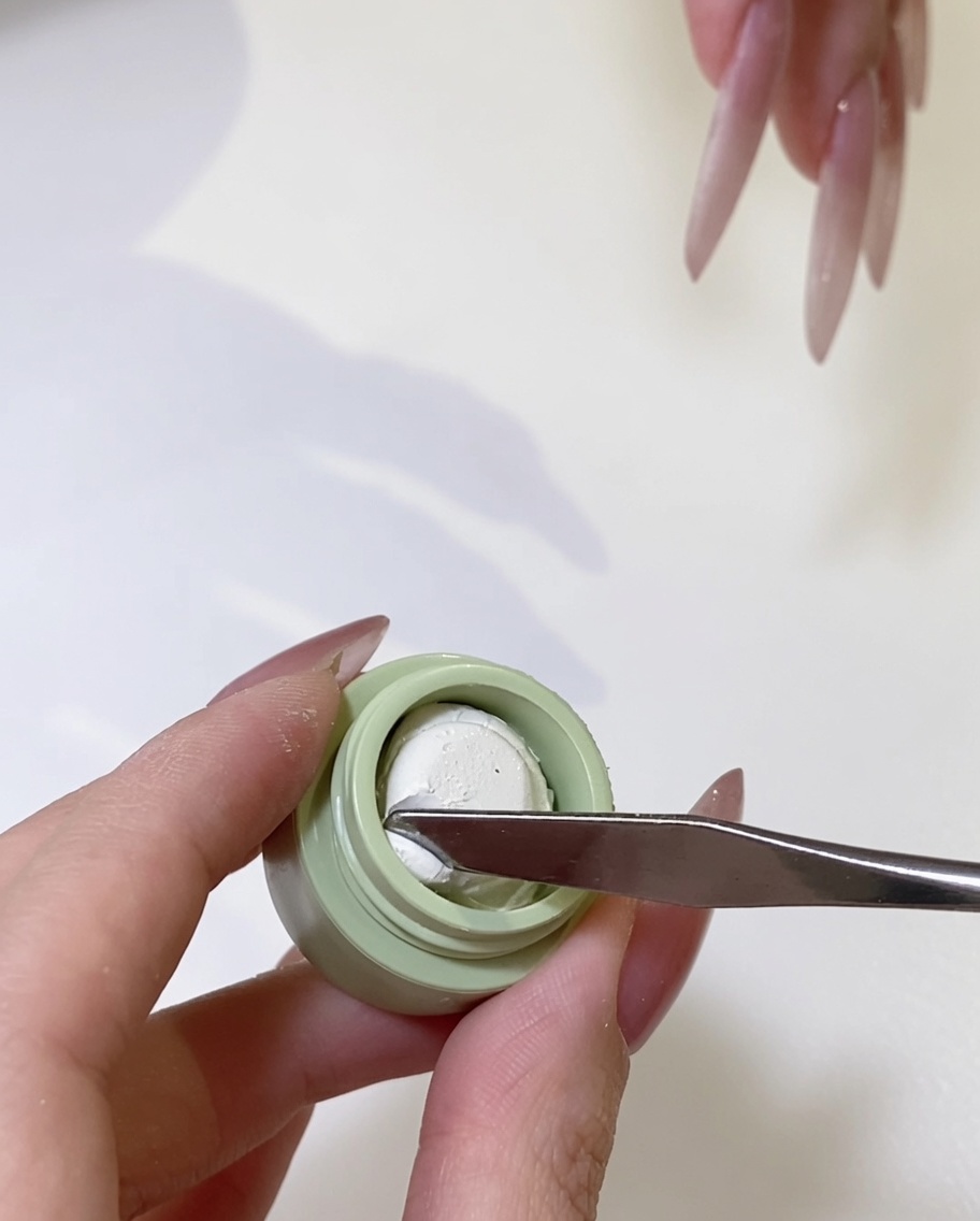 Gros plan sur une spatule en métal prélevant une petite quantité de gel ivoire dans son pot.