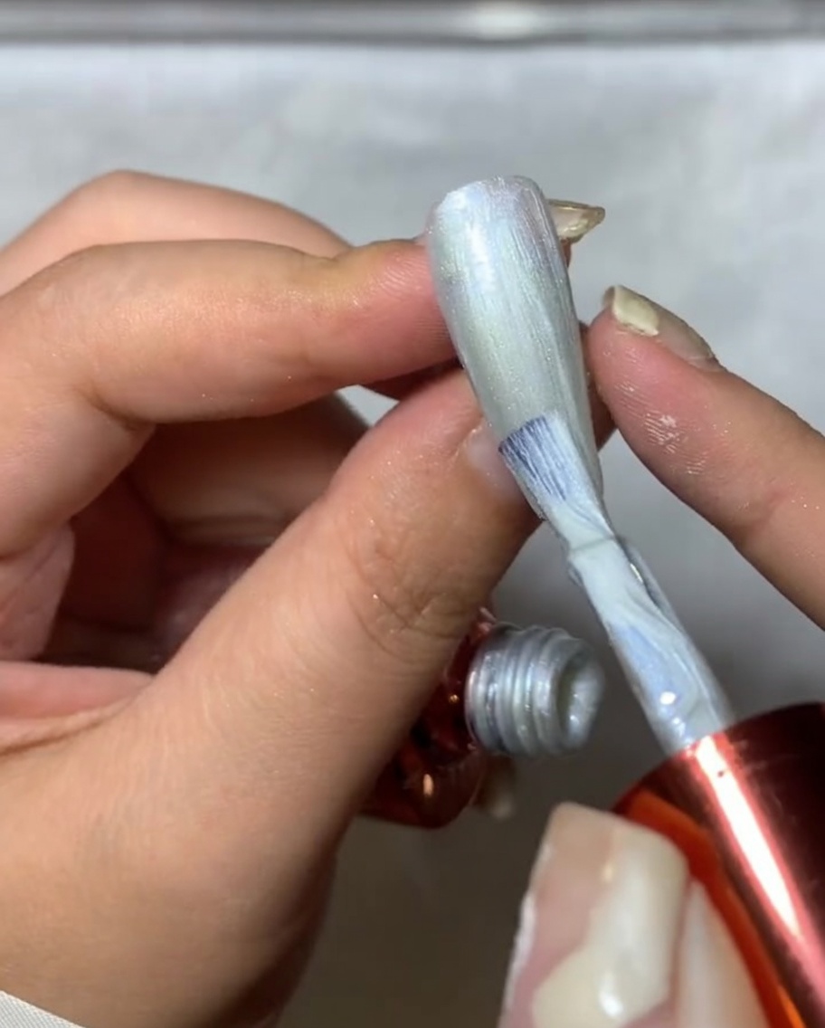 Gros plan dun pinceau à ongles appliquant du spider gel argenté sur un ongle, créant des lignes fines et texturées ressemblant à une toile.
