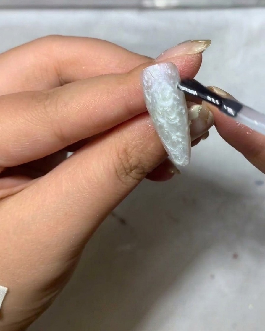 Un pinceau liner fin commençant à peindre des pétales de marguerite blancs délicats sur une surface dongle grise mate.