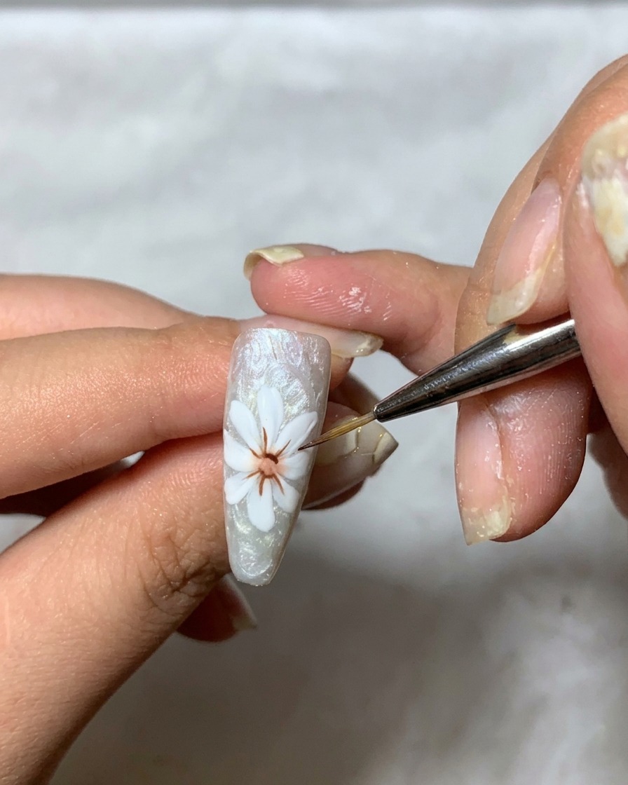 Un pinceau fin appliquant un gel transparent épais sur le design de pétale blanc sur longle pour construire la dimension.