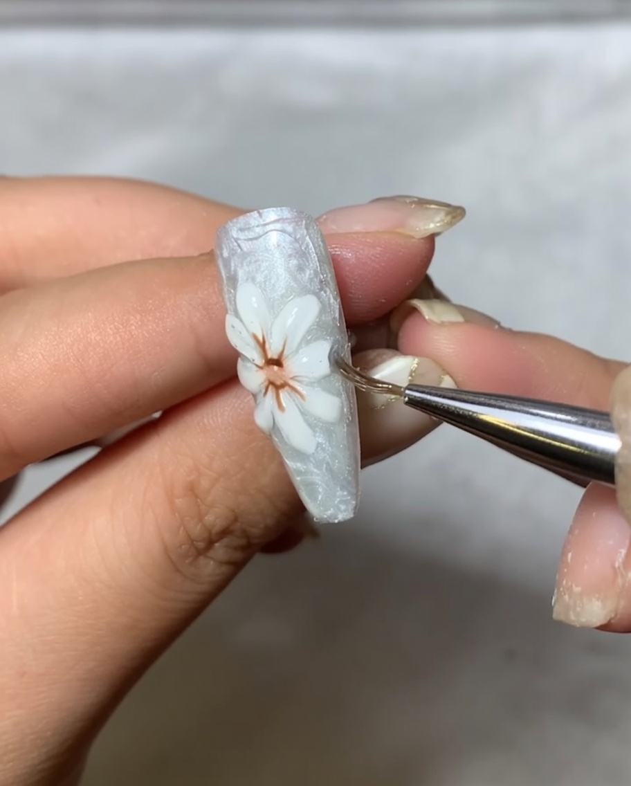 Un pinceau applicateur polissant doucement de la poudre miroir métallique sur les pétales blancs surélevés du nail art.