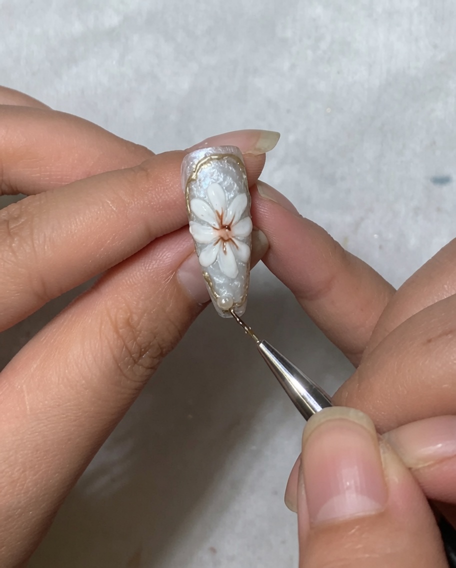 Un outil de nail art plaçant une petite perle blanche près de la zone de la cuticule dun ongle décoré dune marguerite.