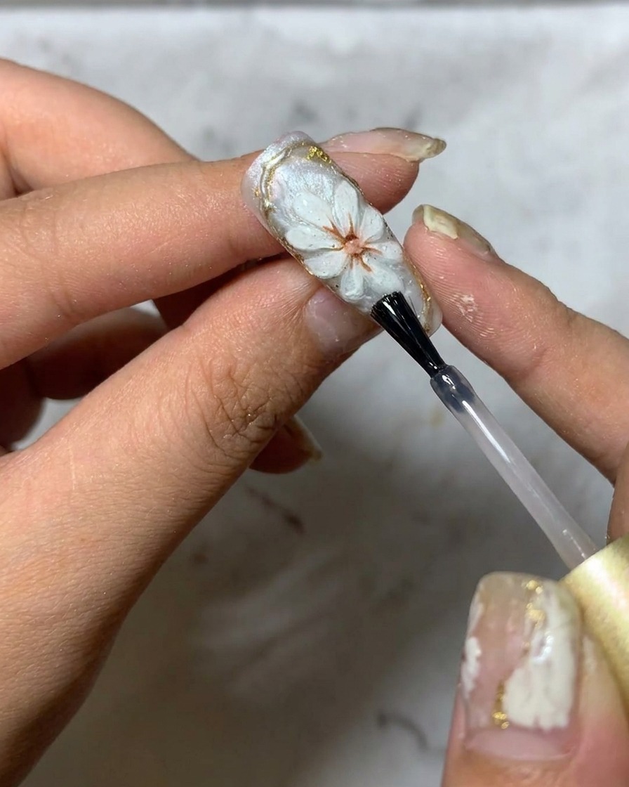 Un pinceau appliquant un top coat brillant final sur un design de nail art marguerite 3D.