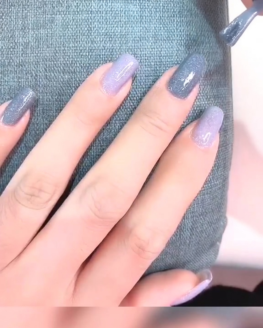 Gros plan sur un ongle avec deux couches de vernis gel gris, paraissant opaque et lisse.