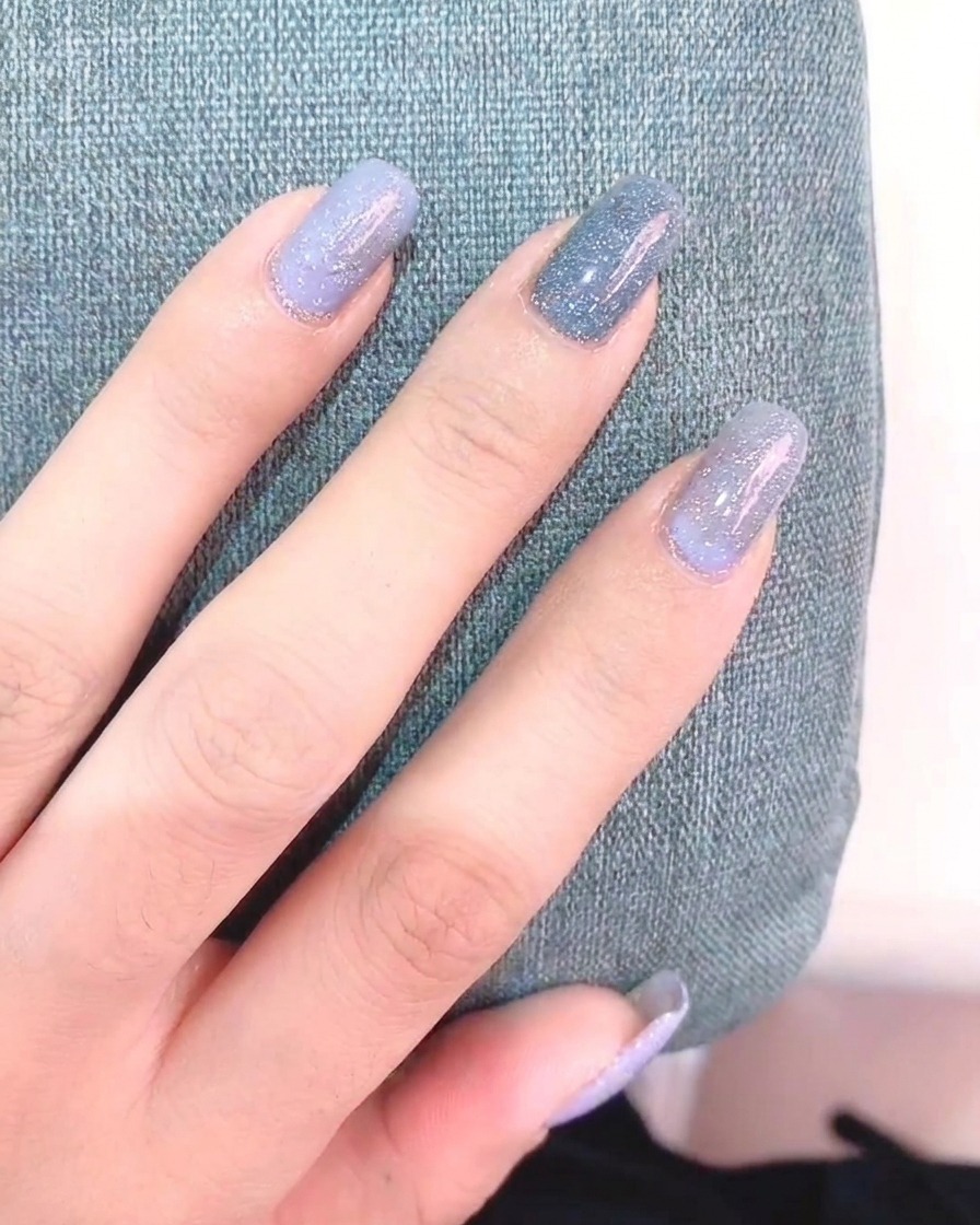 Une main tenant un pinceau liner, peignant des pétales de marguerite blancs sur un ongle gris.