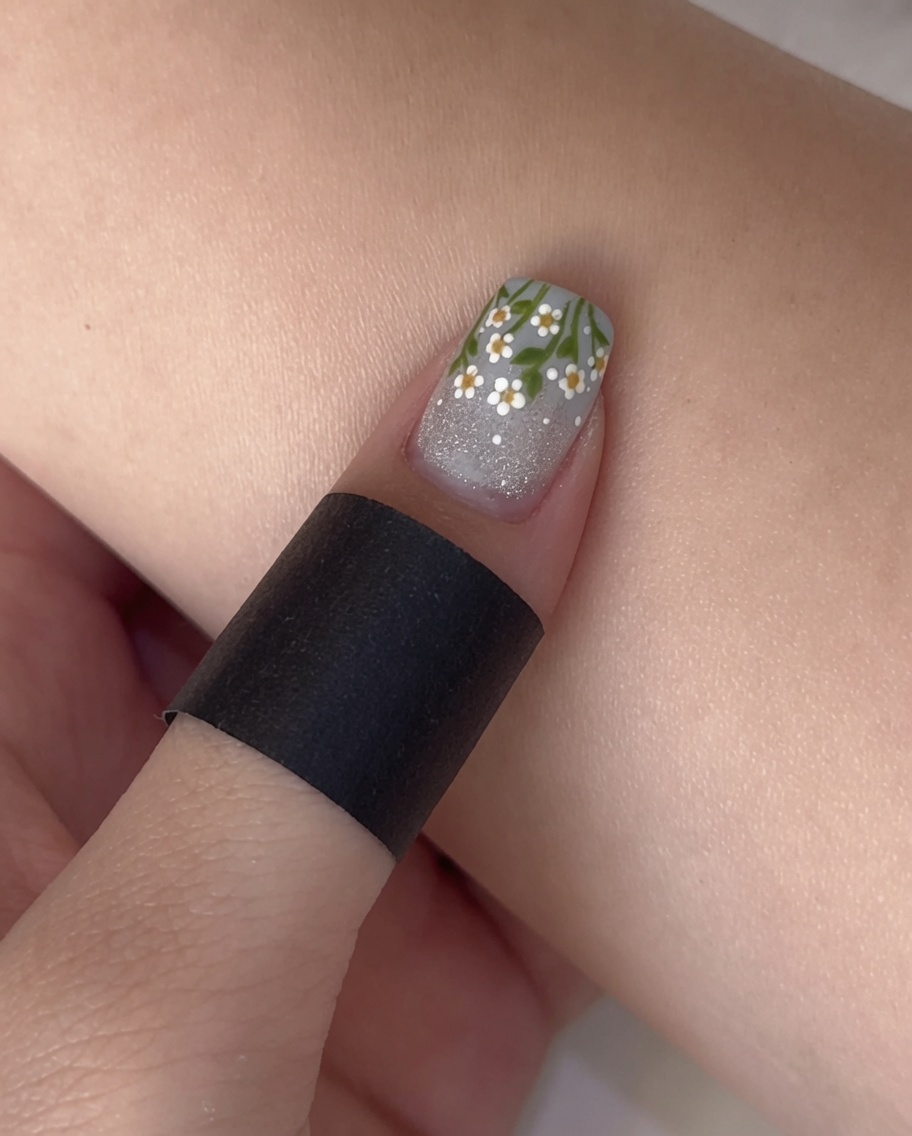 Un pinceau de vernis appliquant un top coat mat transparent sur un ongle avec base pailletée et French bleue.