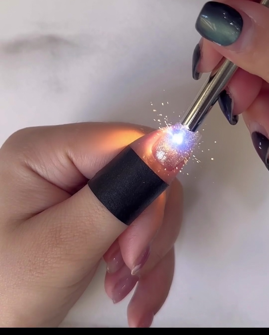 Gros plan dun outil de dotting appliquant du gel jaune au centre dune marguerite blanche en nail art.