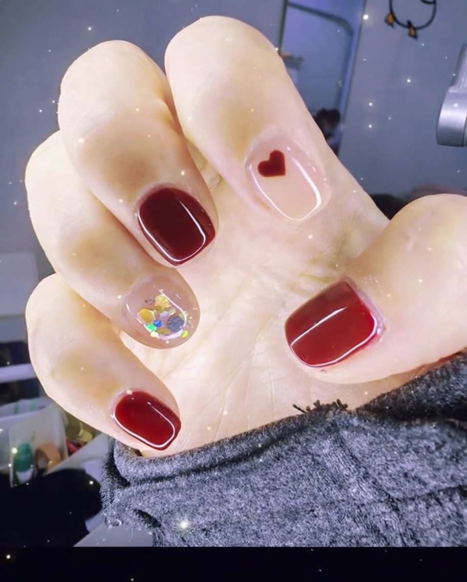 Une pince déposant un petit charme cœur rouge sur la surface dun ongle avec du gel transparent.
