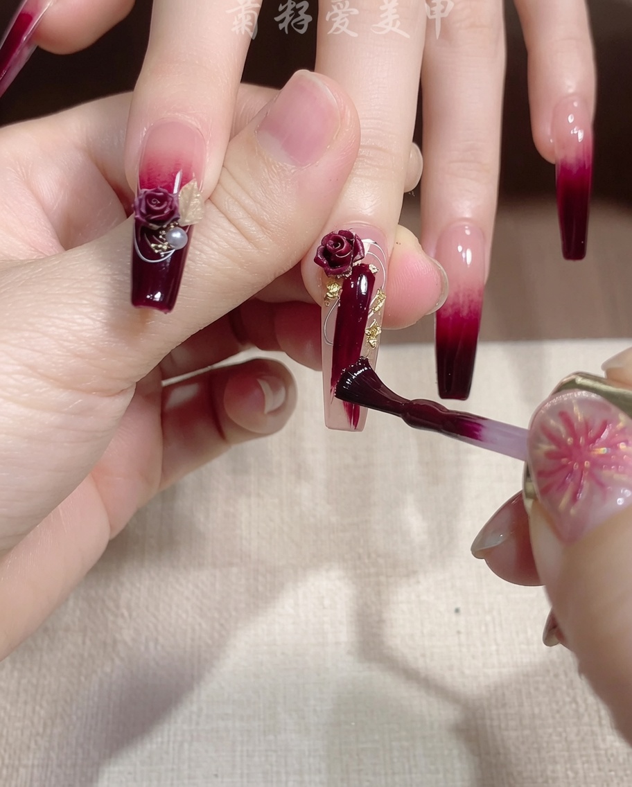 Un pinceau fin appliquant un trait de gel à paillettes dorées sur un ongle rouge.