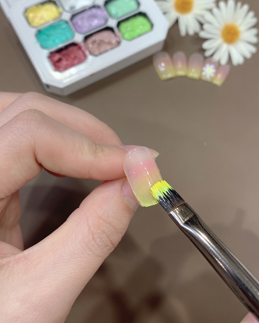 Un pinceau appliquant une fine couche de mélange de gel jaune translucide sur le bord dun ongle dégradé.