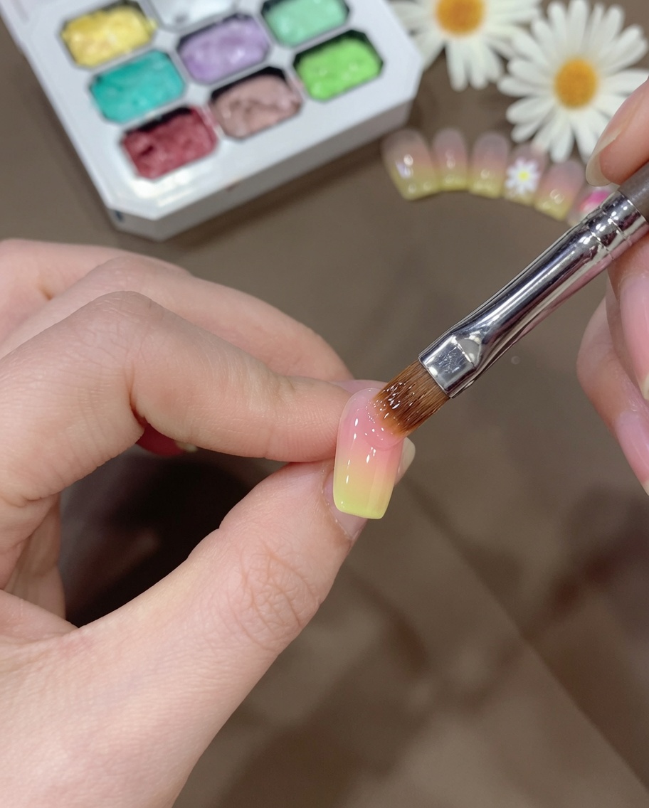 Un pinceau estompant soigneusement la transition du gel jaune sur longle pour créer un dégradé lisse.