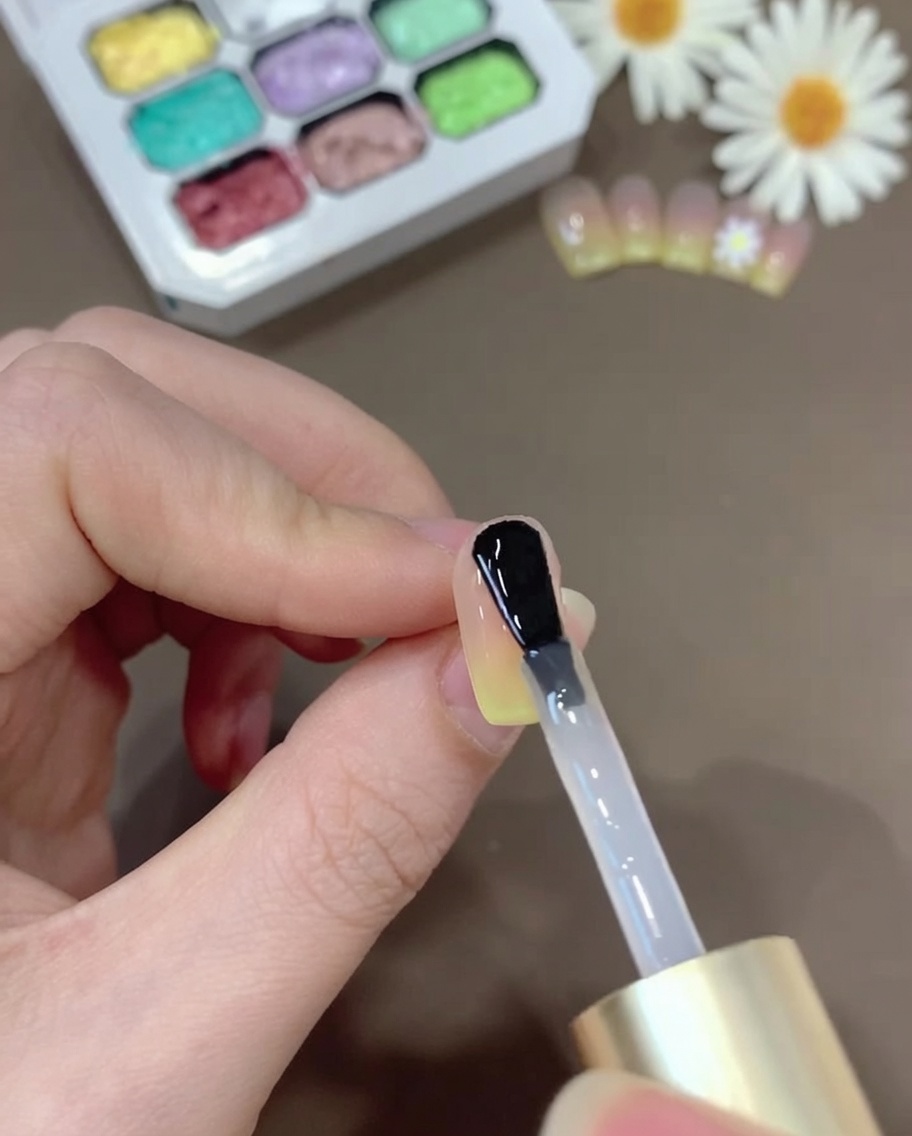 Un pinceau appliquant une couche de gel top coat transparent sur longle dégradé pour offrir une finition brillante.
