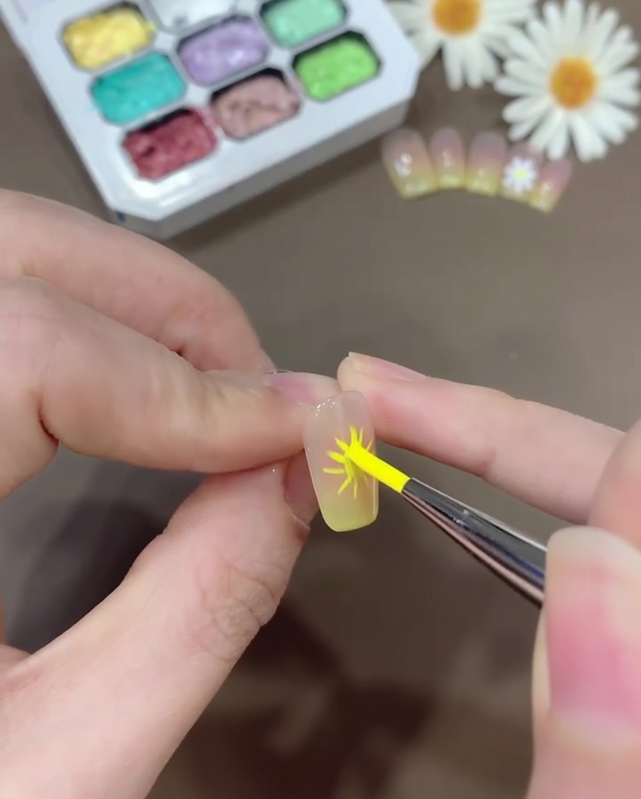Un pinceau nail art appliquant du gel blanc pour former des pétales arrondis en forme de marguerite sur les guides préalablement tracés.