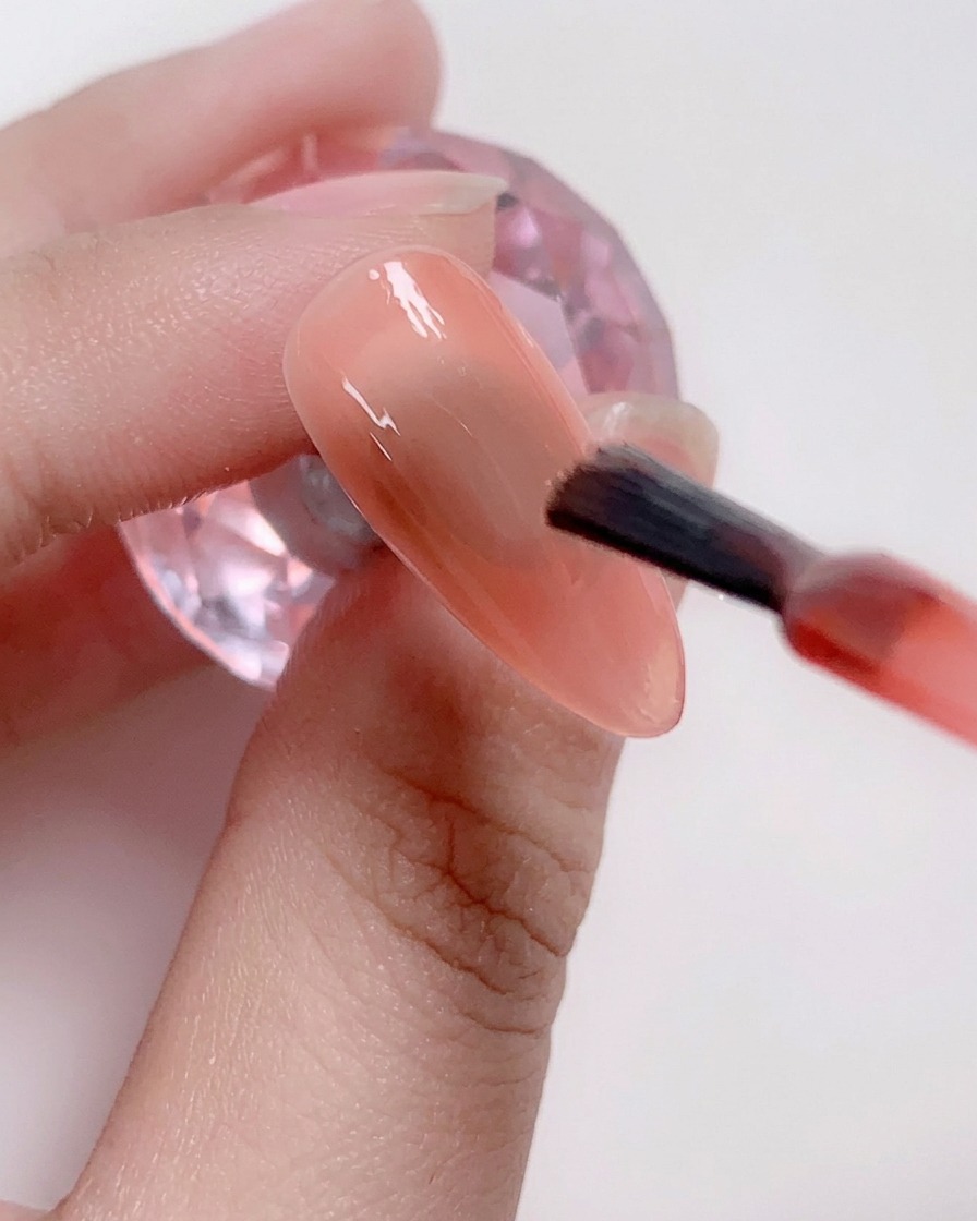 Un pinceau appliquant une couche de vernis gel rose tendre au centre de longle.