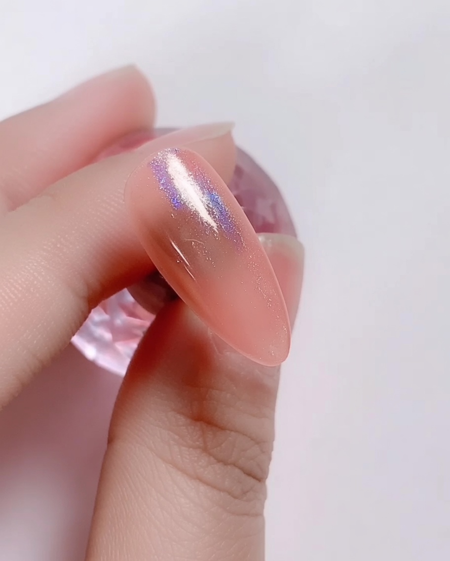 Un petit applicateur mousse frottant de la poudre laser iridescente sur longle en gel rose.