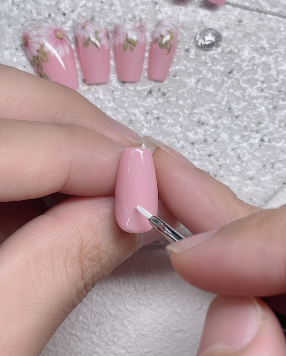 Gros plan dun pinceau liner appliquant un trait de pétale blanc sur un ongle recouvert de gel rose.