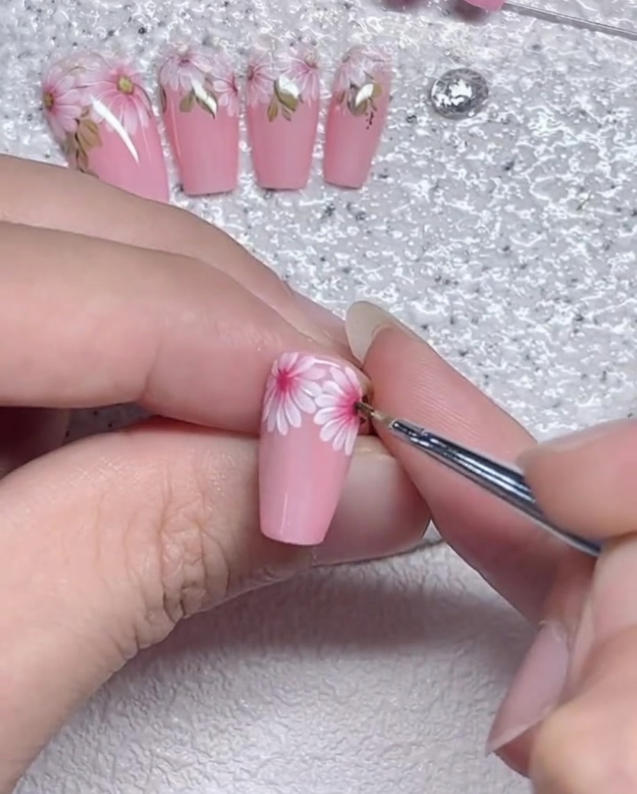 Gros plan dun pinceau liner affinant les bords des pétales de marguerite sur un ongle.