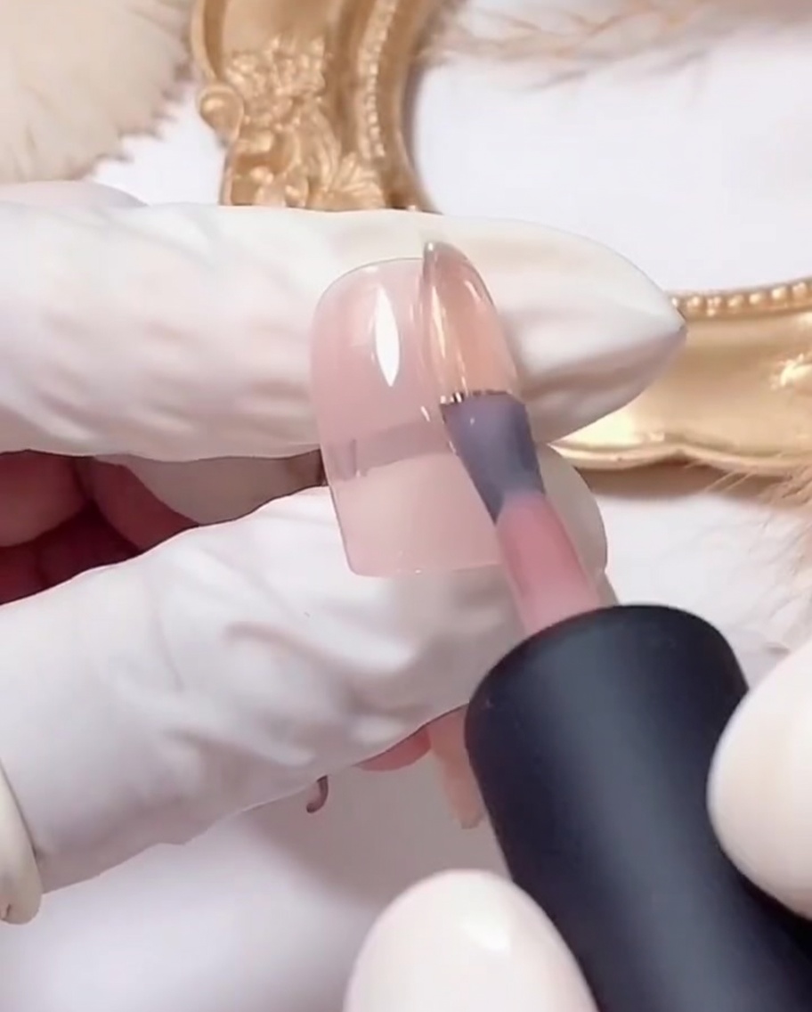 Un pinceau plat déposant du gel à paillettes argentées sur le bout dun ongle rose.