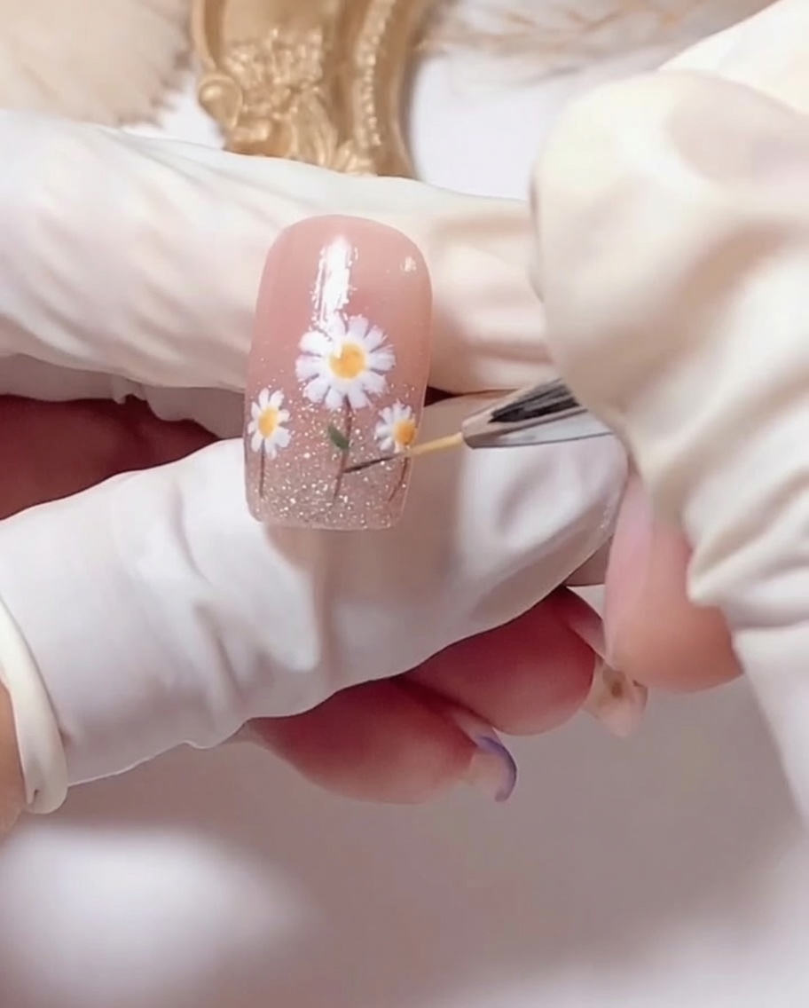 Un pinceau appliquant un top coat transparent brillant sur le nail art marguerite terminé.