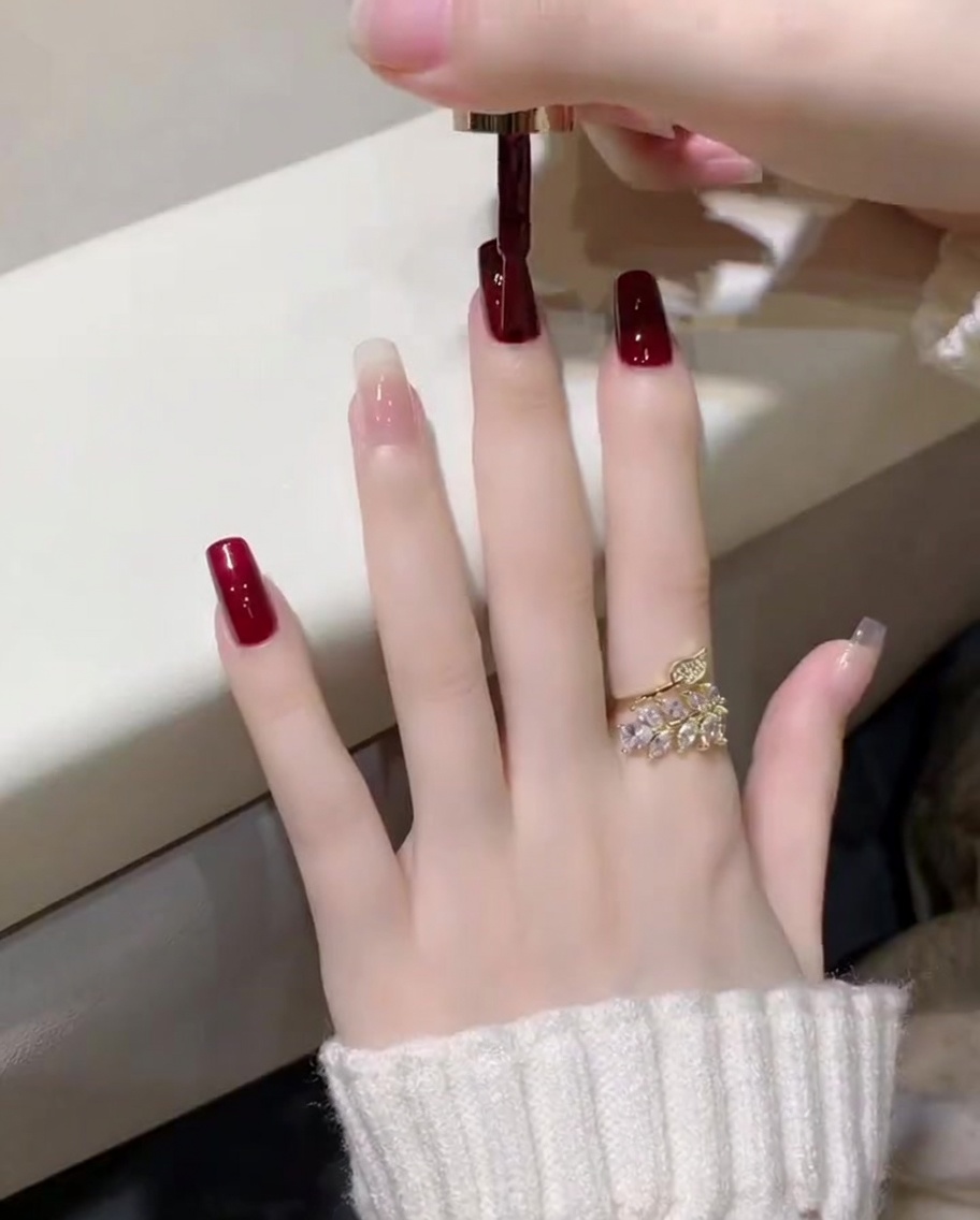 Gros plan sur lapplication dun vernis gel rouge vin profond avec un pinceau sur un ongle de pouce.