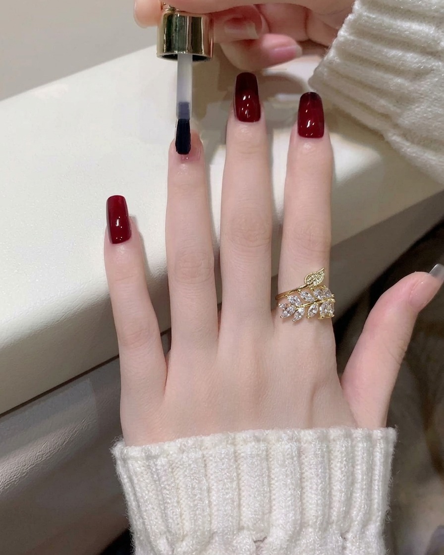 Gros plan sur lapplication dune deuxième couche de vernis gel rouge vin sur lindex.