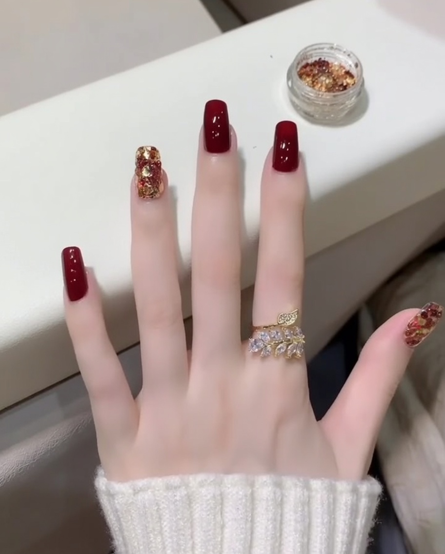 Gros plan sur un pinceau appliquant un top coat transparent et brillant sur des ongles rouge foncé et pailletés.