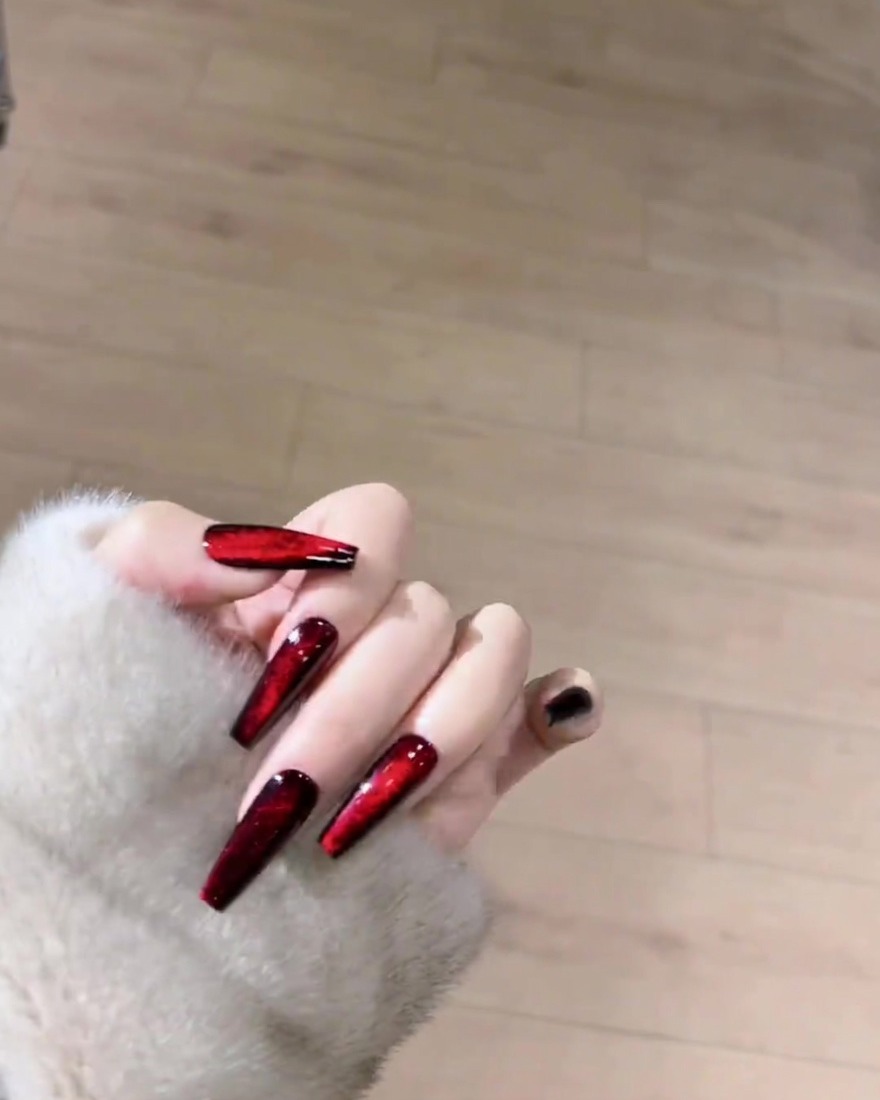 Un aimant positionné au-dessus dun ongle enduit de gel rouge humide pour sculpter les reflets en une ligne.