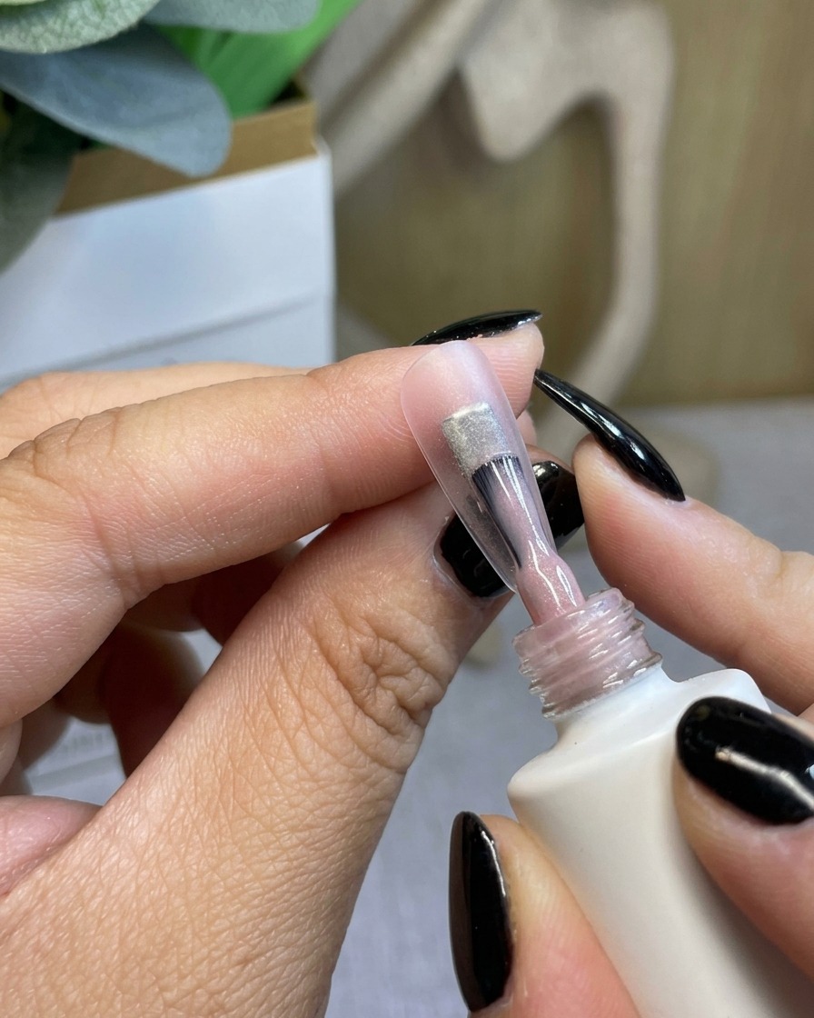 Un pinceau appliquant une base coat transparente sur un ongle naturel.