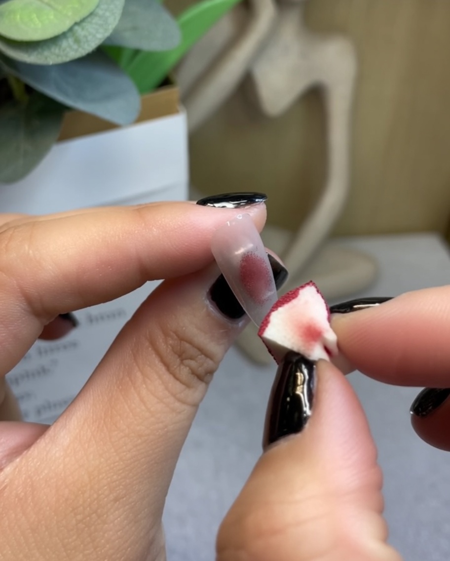 Une éponge de maquillage tamponnant du gel rouge vin au centre dun ongle.