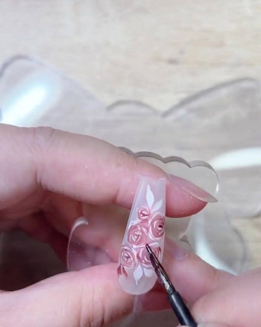 Détail du pinceau appliquant un gel rouge profond pour rehausser les ombres et la structure des pétales.