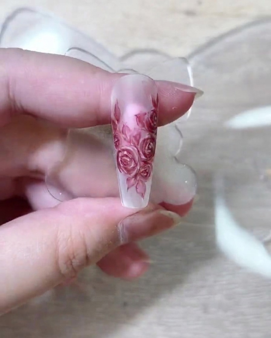 Un pinceau nail art fin déposant du pigment rouge foncé sur les pétales superposés.
