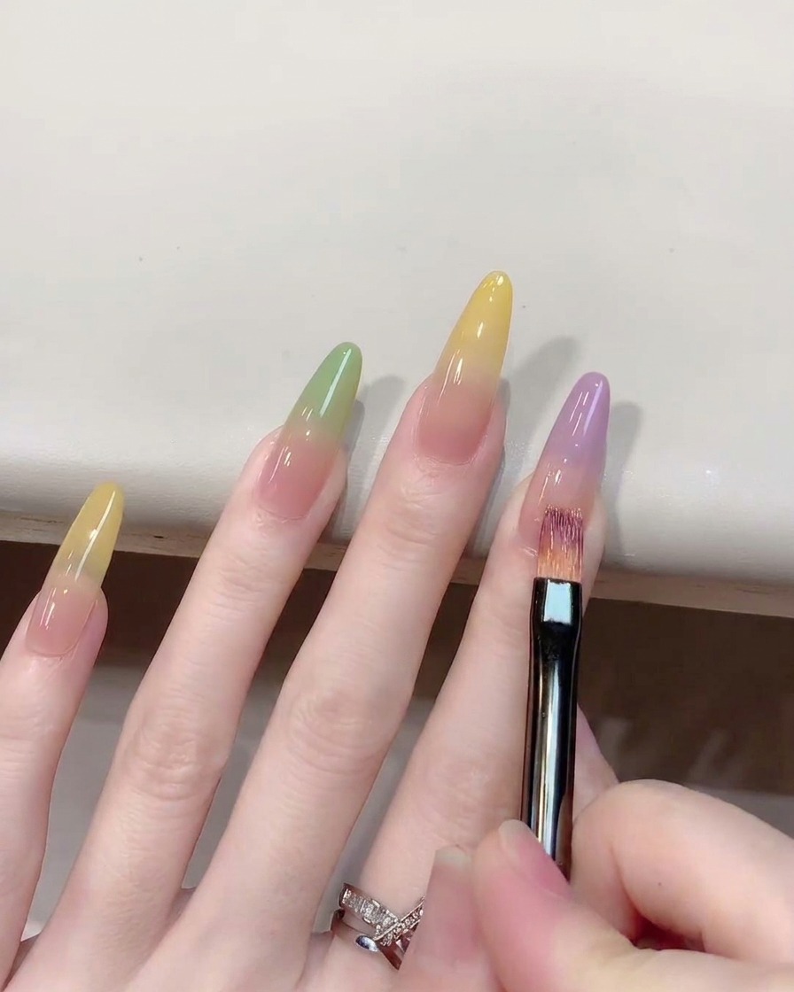Gros plan montrant un pinceau ombré estompant du gel violet vers le haut sur un ongle.
