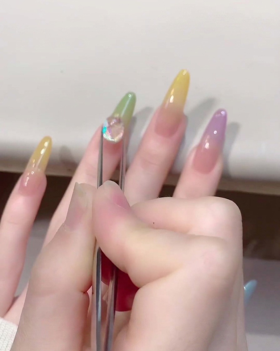 Gros plan dune pince à épiler posant un charm brillant en forme de cœur en cristal transparent sur un ongle de couleur jelly.