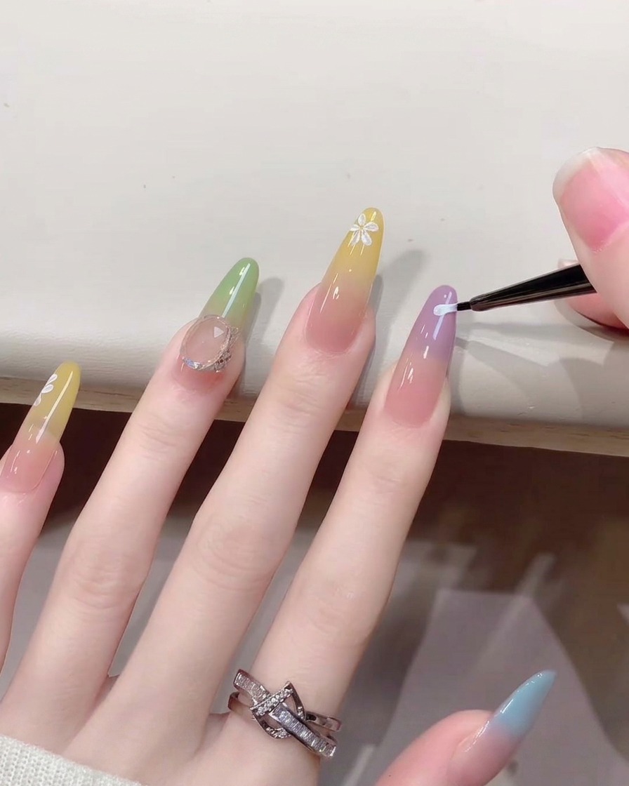 Gros plan dun pinceau fin pour nail art peignant de minuscules pétales de fleurs blancs sur un ongle au design dégradé.