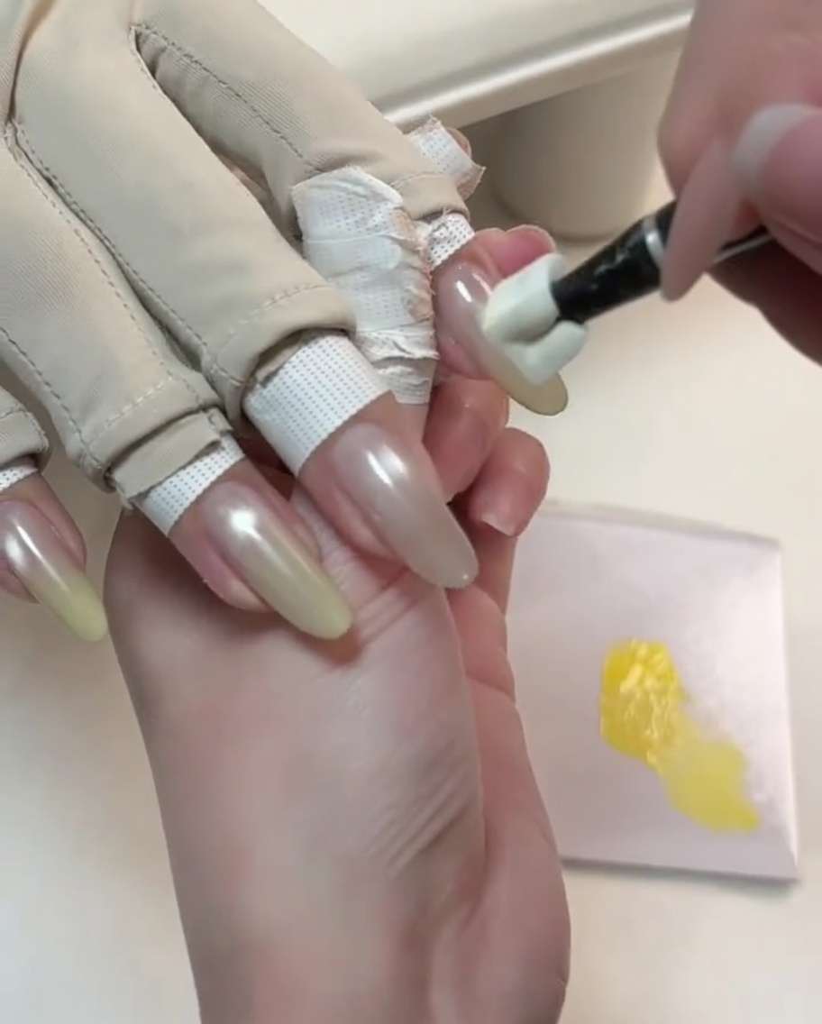 Un outil spécial tamponnant du gel jaune sur la pointe dun ongle nude cat-eye.