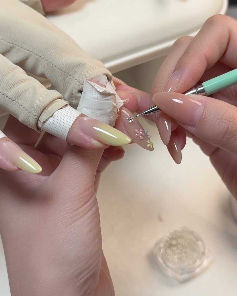 Un outil de précision plaçant une petite perle au centre dun nail art floral sur un ongle en amande.